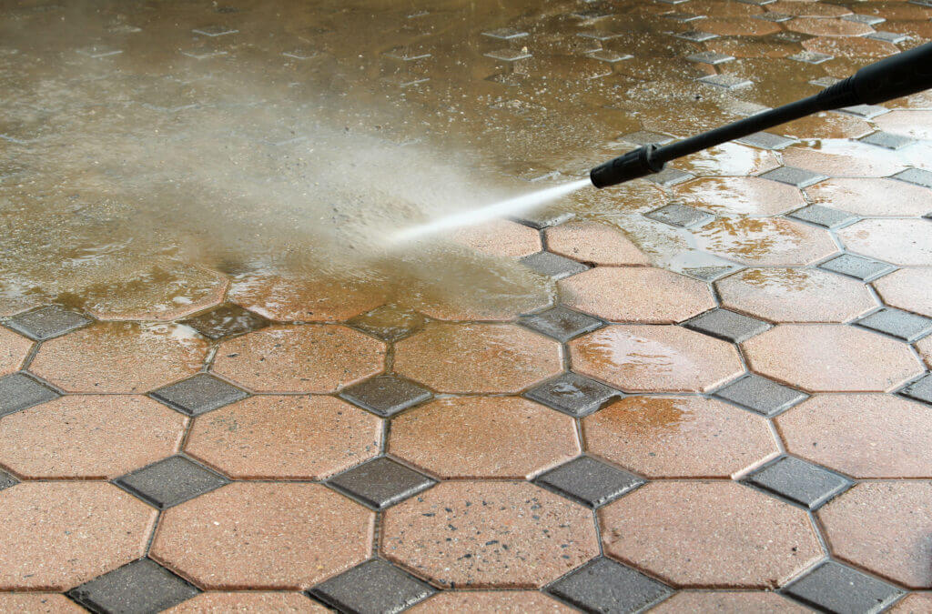 Close-up of a pressure washing tool spraying a powerful jet of water to remove dirt and grime from a tile patio surface.