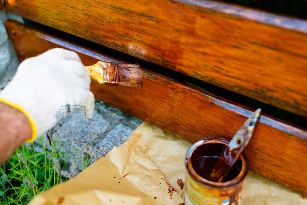 Professional staining a wooden backyard fence in natural sunlight. HAND STAINED DECK CARE BY BLUE MONKEY