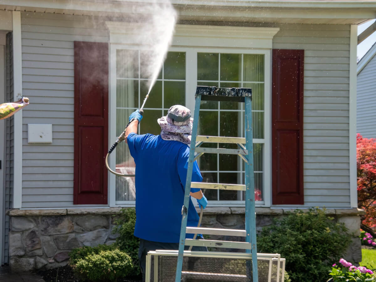 A man using a power washer to clean the windows and front exterior of a house, removing dirt and buildup.