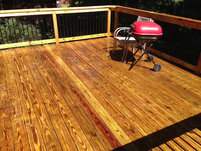 Backyard wooden deck with iron railing and grill, freshly pressure washed, stained, and sealed by Blue Monkey, ready for guests.