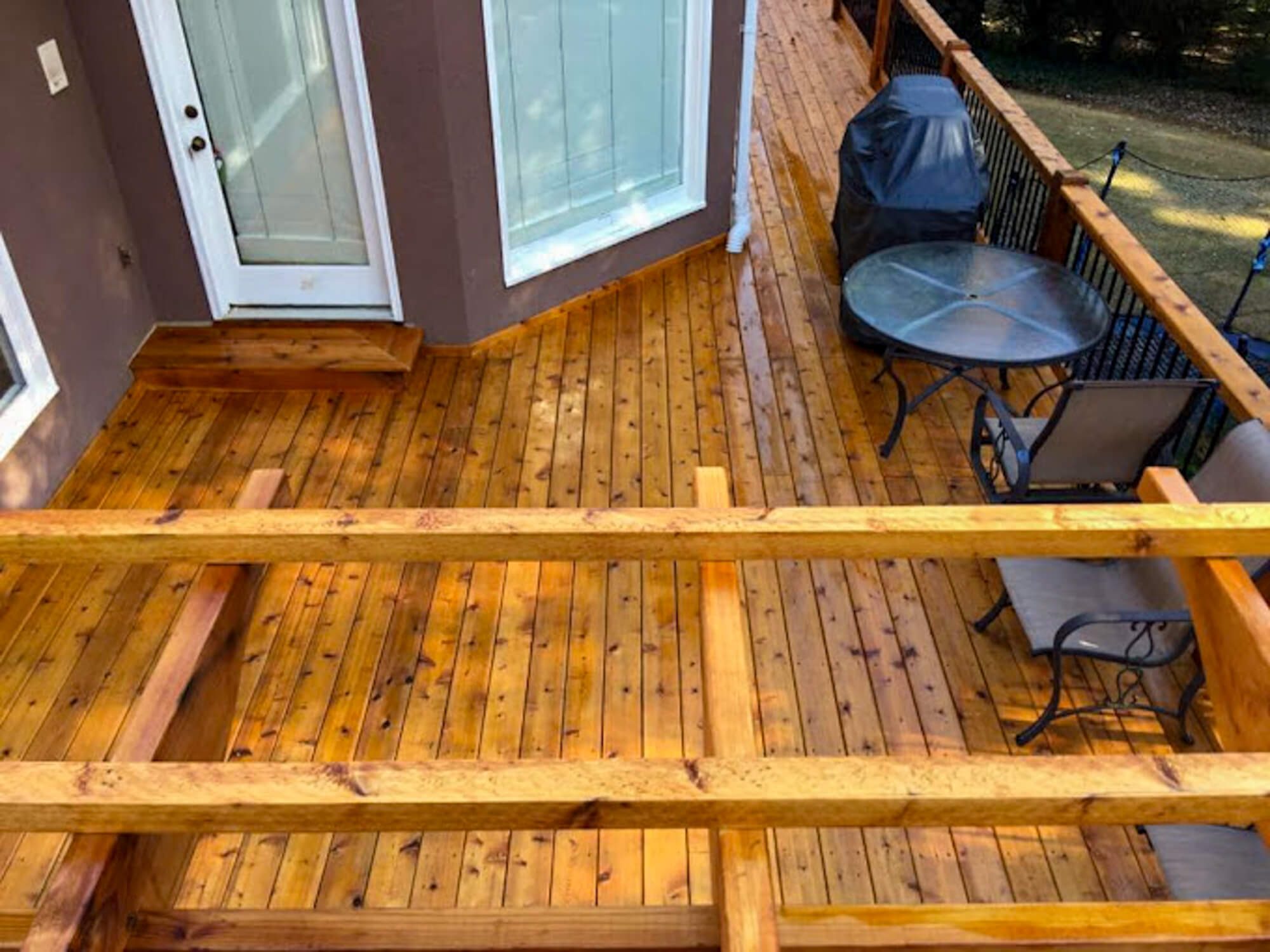 Beautifully hand-stained wooden deck with wrought iron railing and pergola after a professional deck pressure washing service.