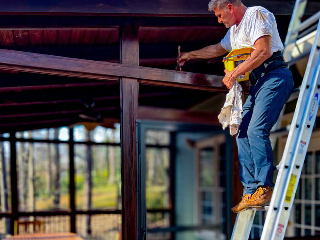 Expert Deck Staining & Restoration Services - MAN HAND BRUSHING STAINING THE TOP OF AN EXTERIOR DOOR FRAME