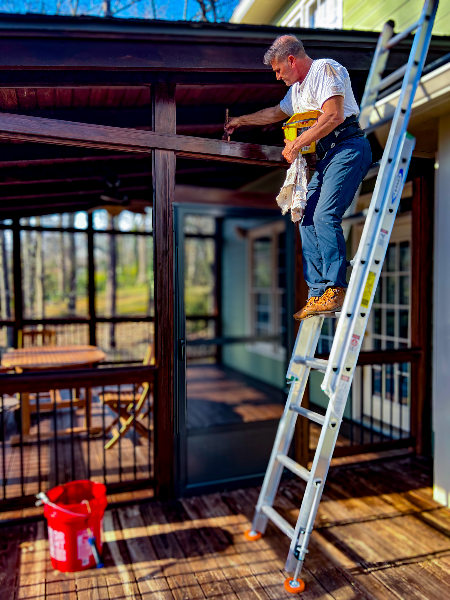 Expert Deck Staining & Restoration Services - MAN HAND BRUSHING STAINING THE TOP OF AN EXTERIOR DOOR FRAME
