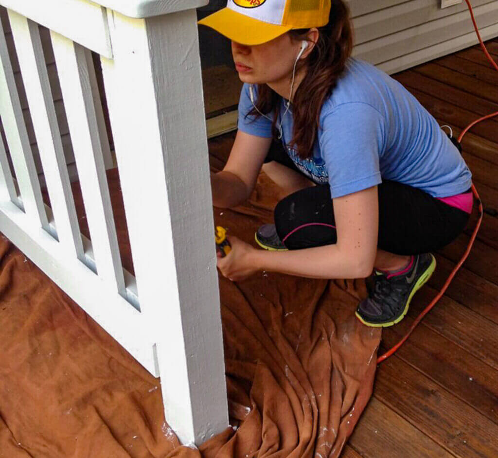 Woman repairing and painting a wooden deck railing as part of a deck restoration project to enhance durability and curb appeal.
