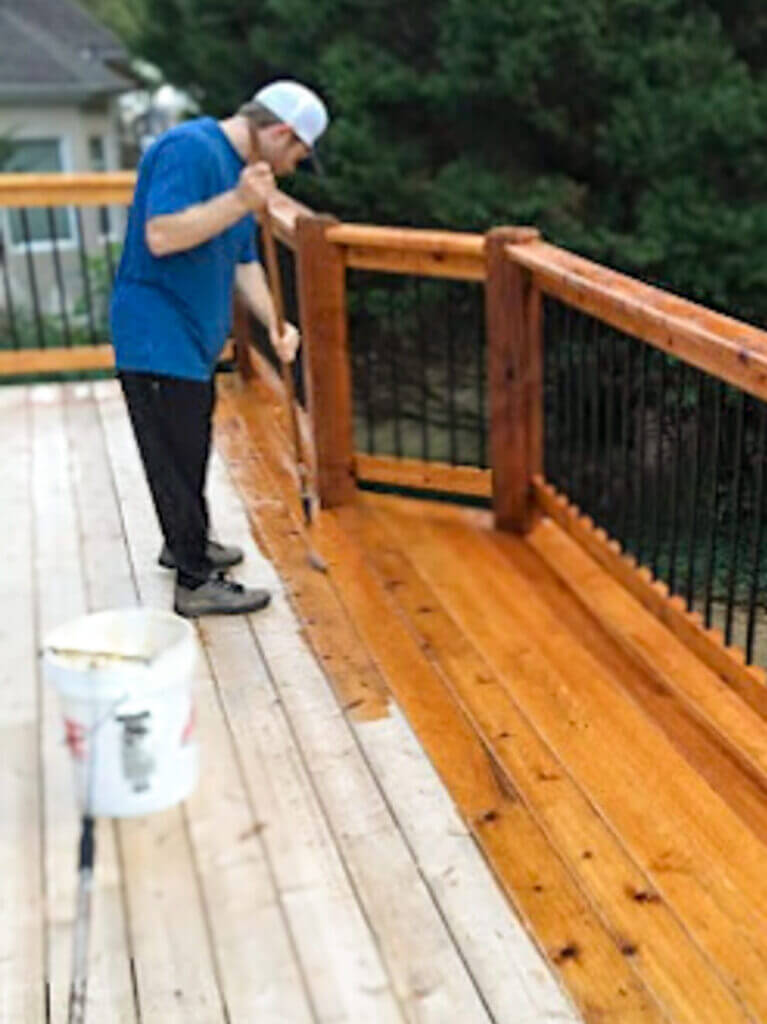 Expert Deck Staining & Restoration Services - MAN HAND BRUSHING STAINING THE TOP OF A backyard deck