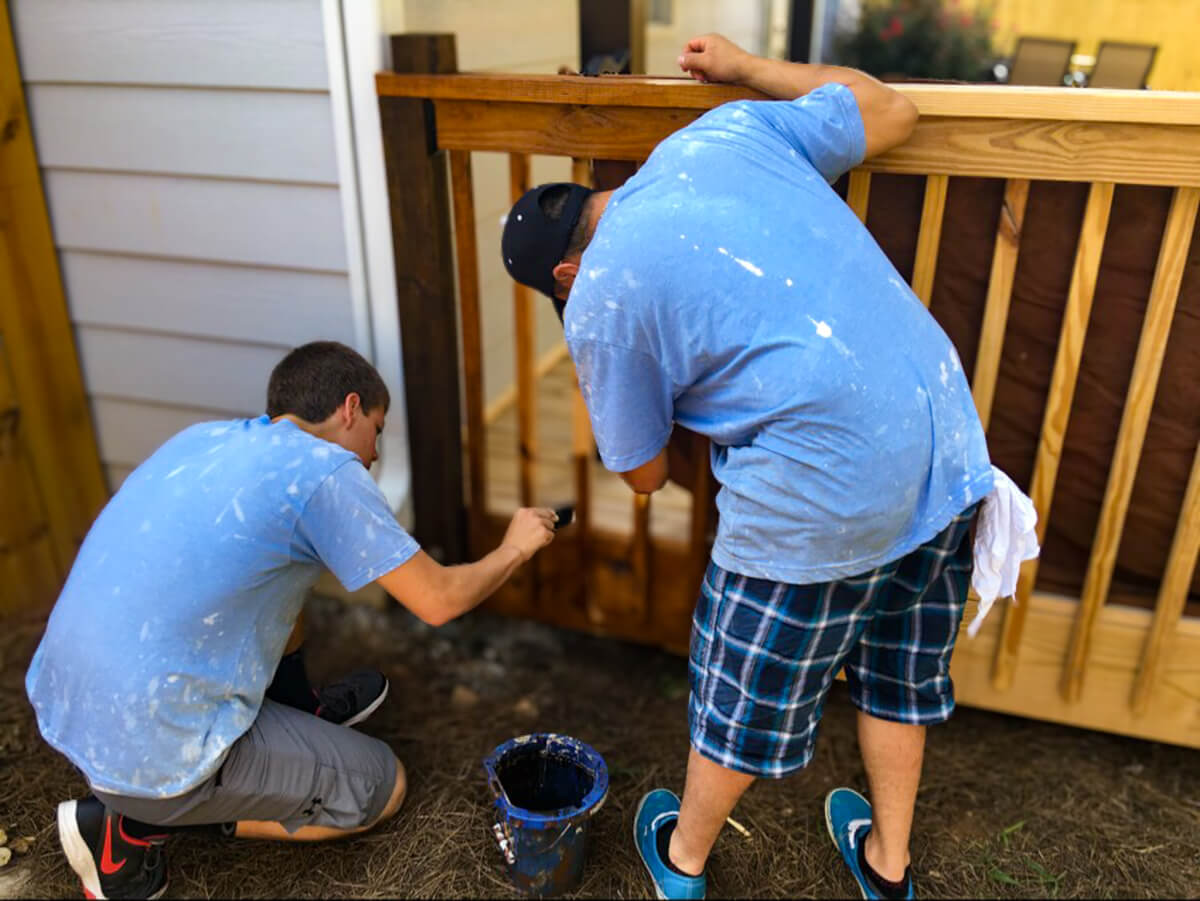 Two men staining and restoring a wooden deck railing, enhancing its durability and appearance with a professional finish.