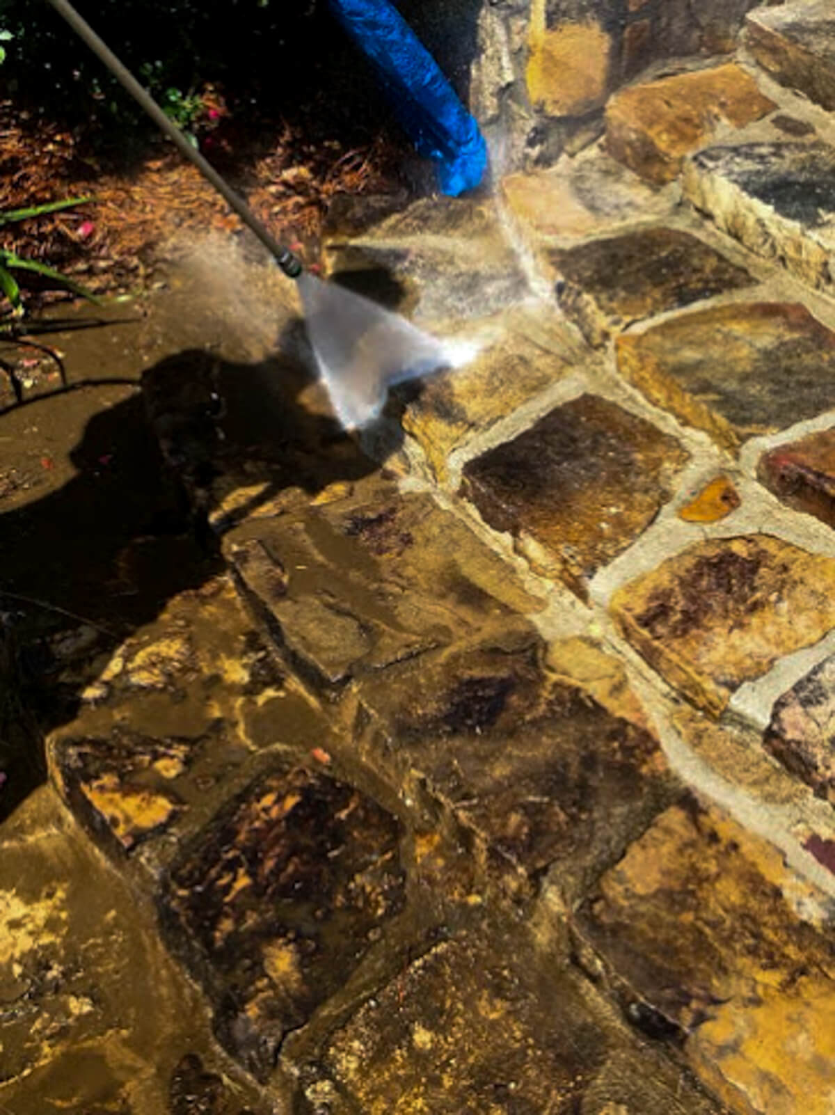 Close-up of a stone paver patio being pressure washed, removing dirt, grime, and moss to restore its natural color and beauty.
