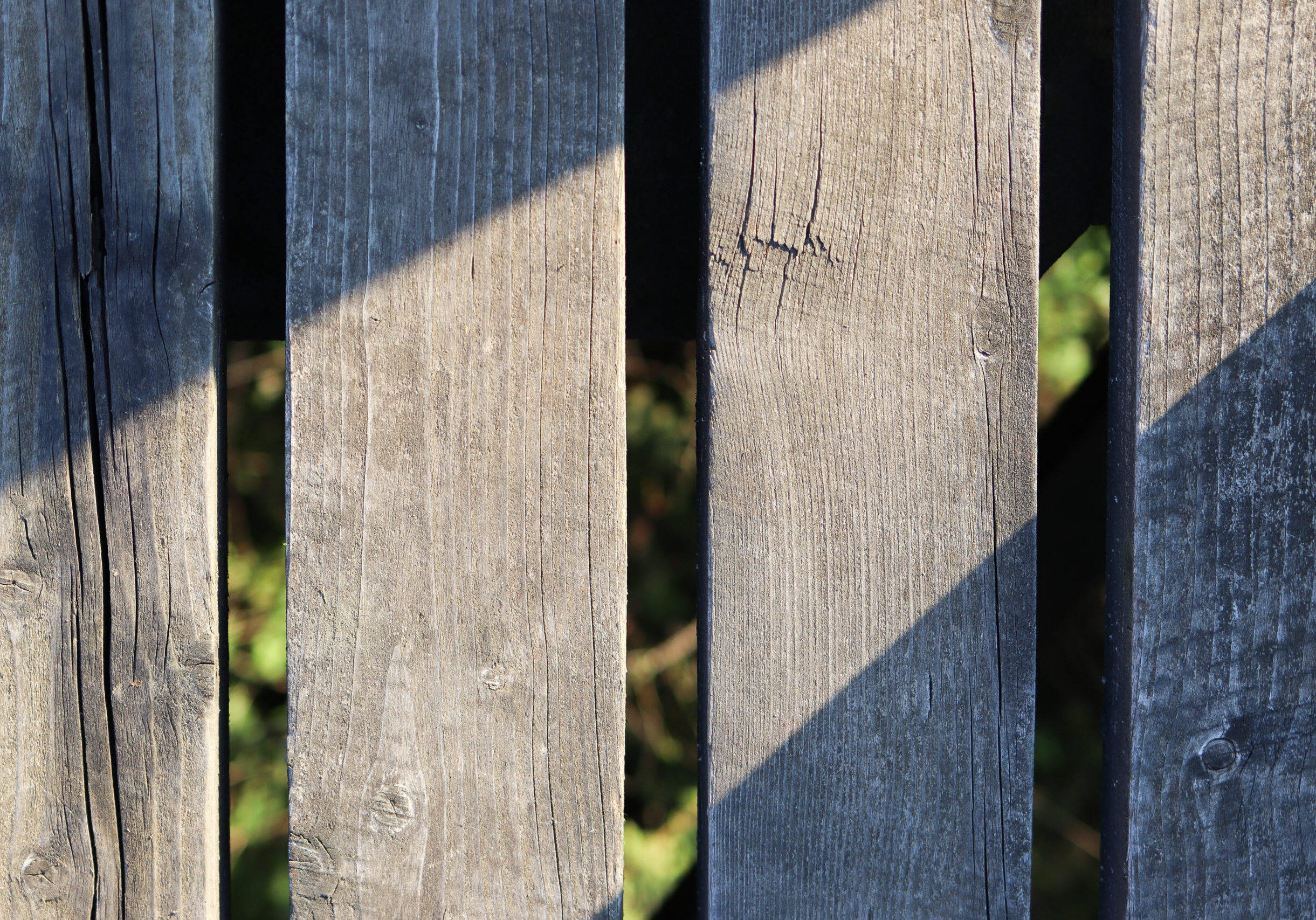 A worn wooden fence with visible cracks and gaps between planks needing fence PRESSURE WASHING & FENCE restoration services