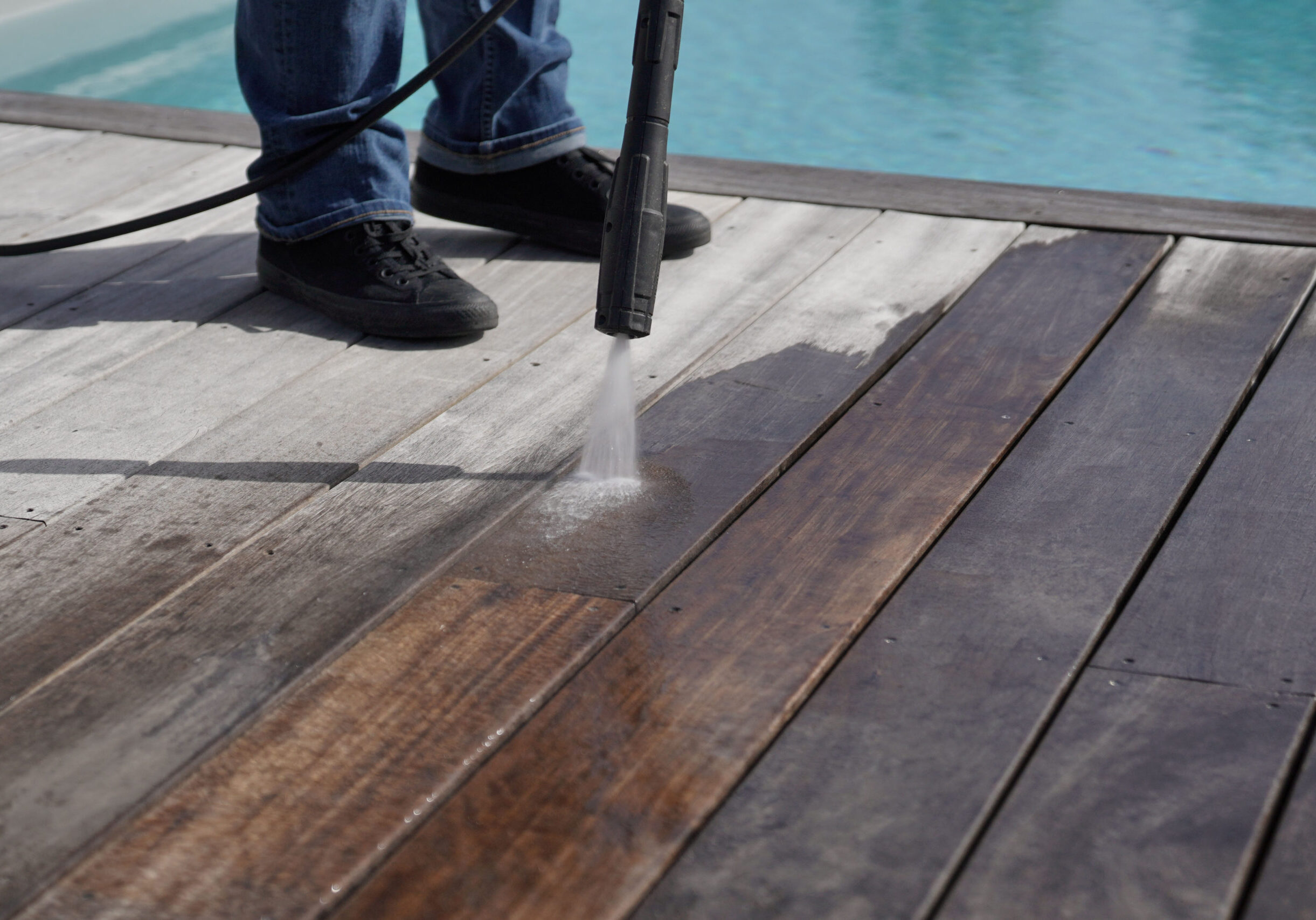 A man pressure washes a wooden pool deck, removing dirt, grime, and algae buildup. PRESSURE WASHING SERVICES LIST