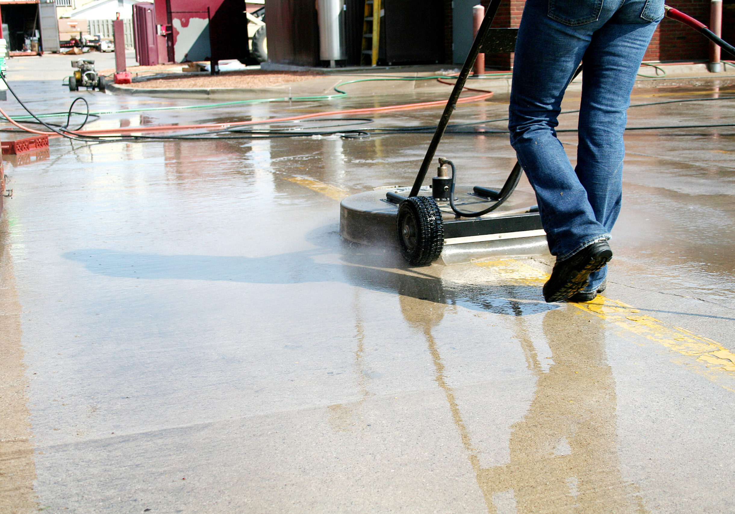 Professional sidewalk pressure washing using a high-powered surface cleaner for deep and uniform cleaning in a commercial area.