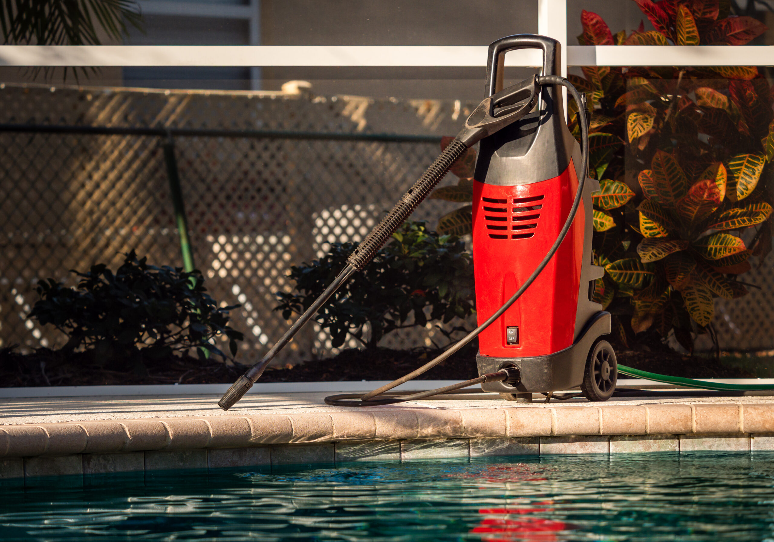 A professional-grade electric pressure washer sits on a concrete pool deck, ready for cleaning.