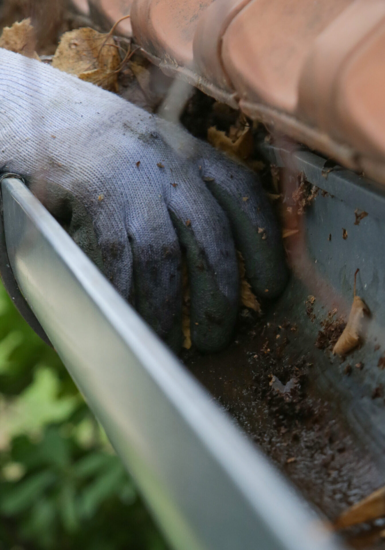 Expert Tips and Tricks for Easy Home Maintenance - Monkey Academy Blog Gloved hand removing leaves and debris from a clogged gutter during a professional gutter cleaning service.