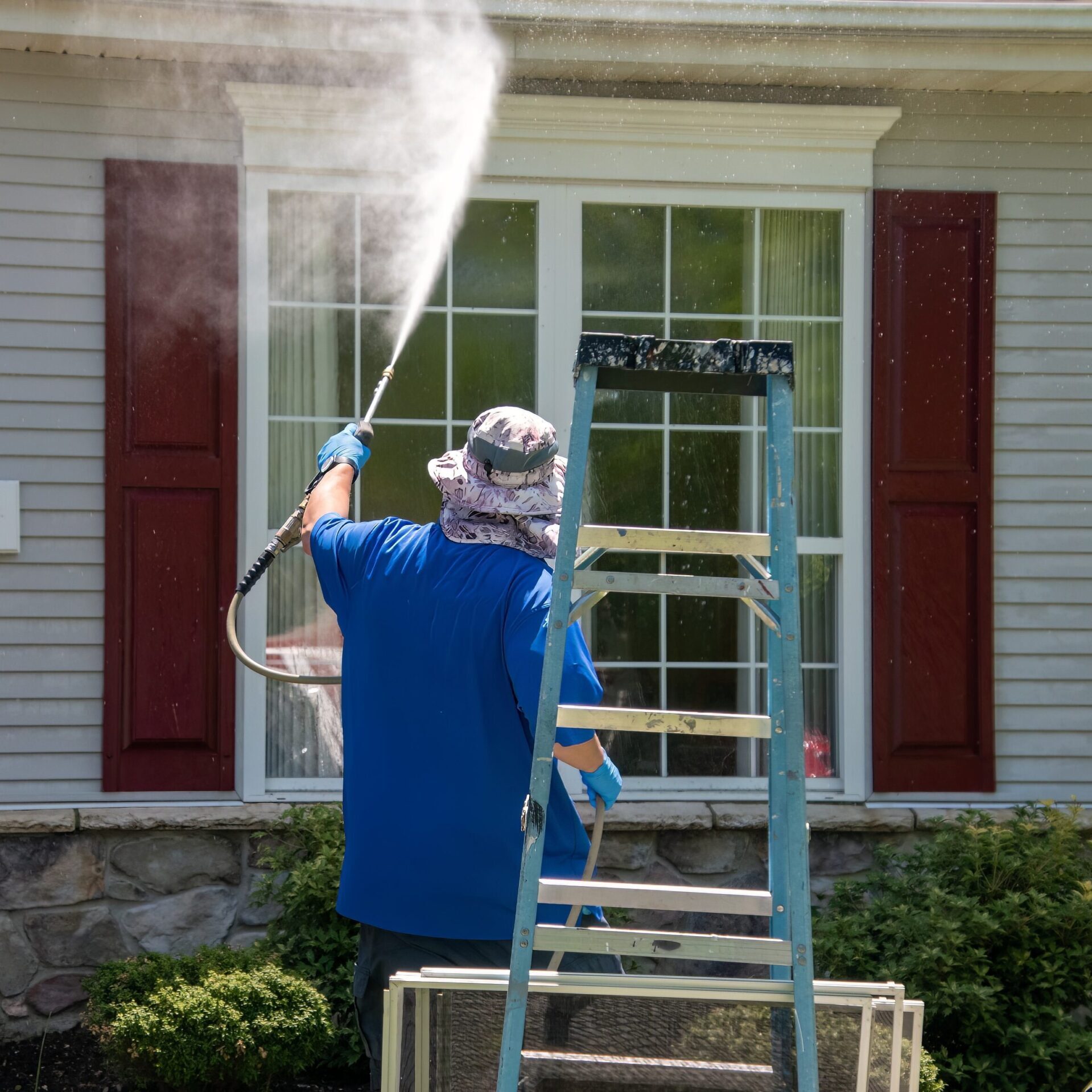 A man using a pressure washer to clean the windows and front exterior of a house, removing dirt and buildup.