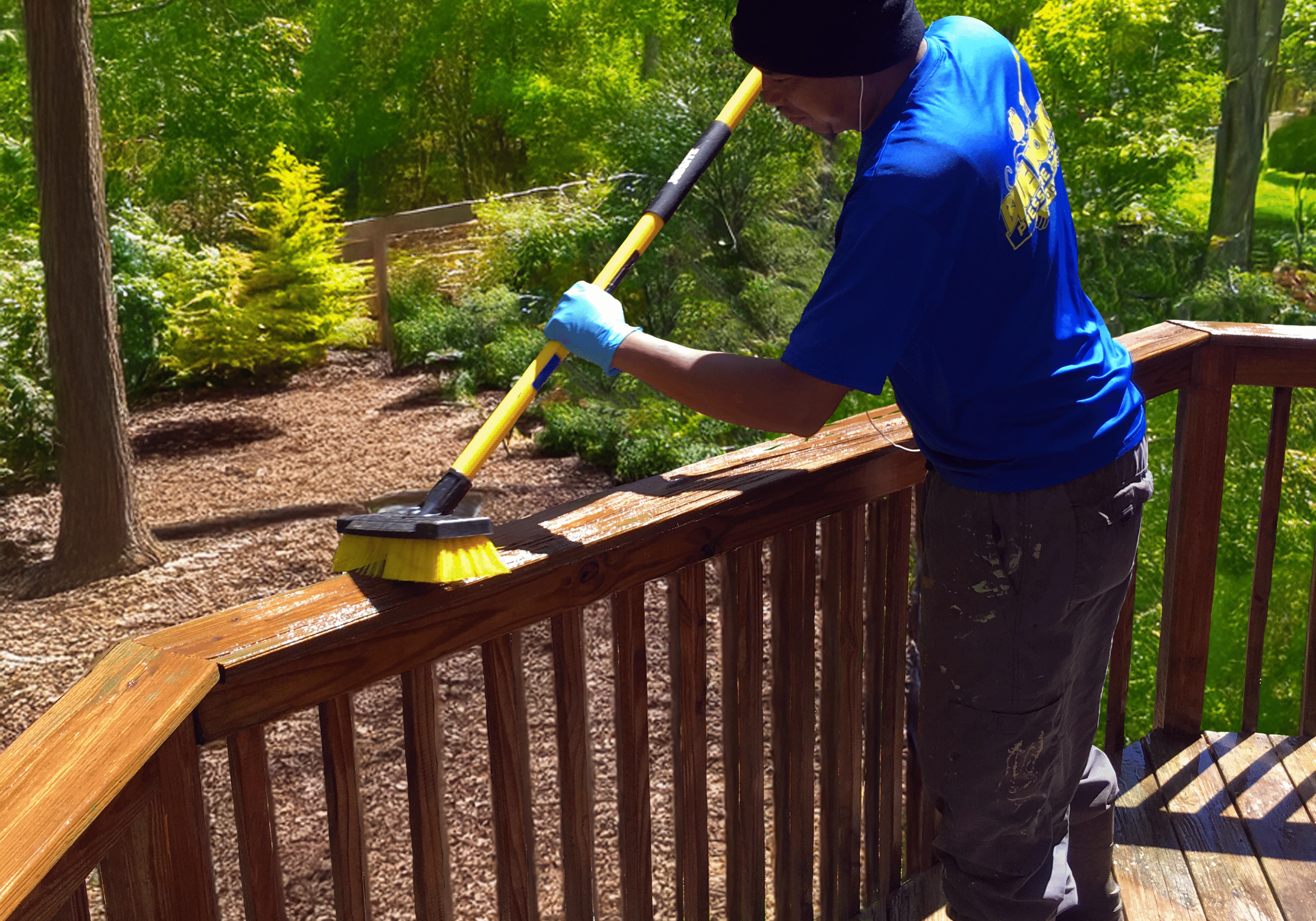 A man carefully hand-brushing stain onto a wooden deck railing, ensuring deep penetration and even coverage during DECK PRESSURE WASH, stain AND seal service