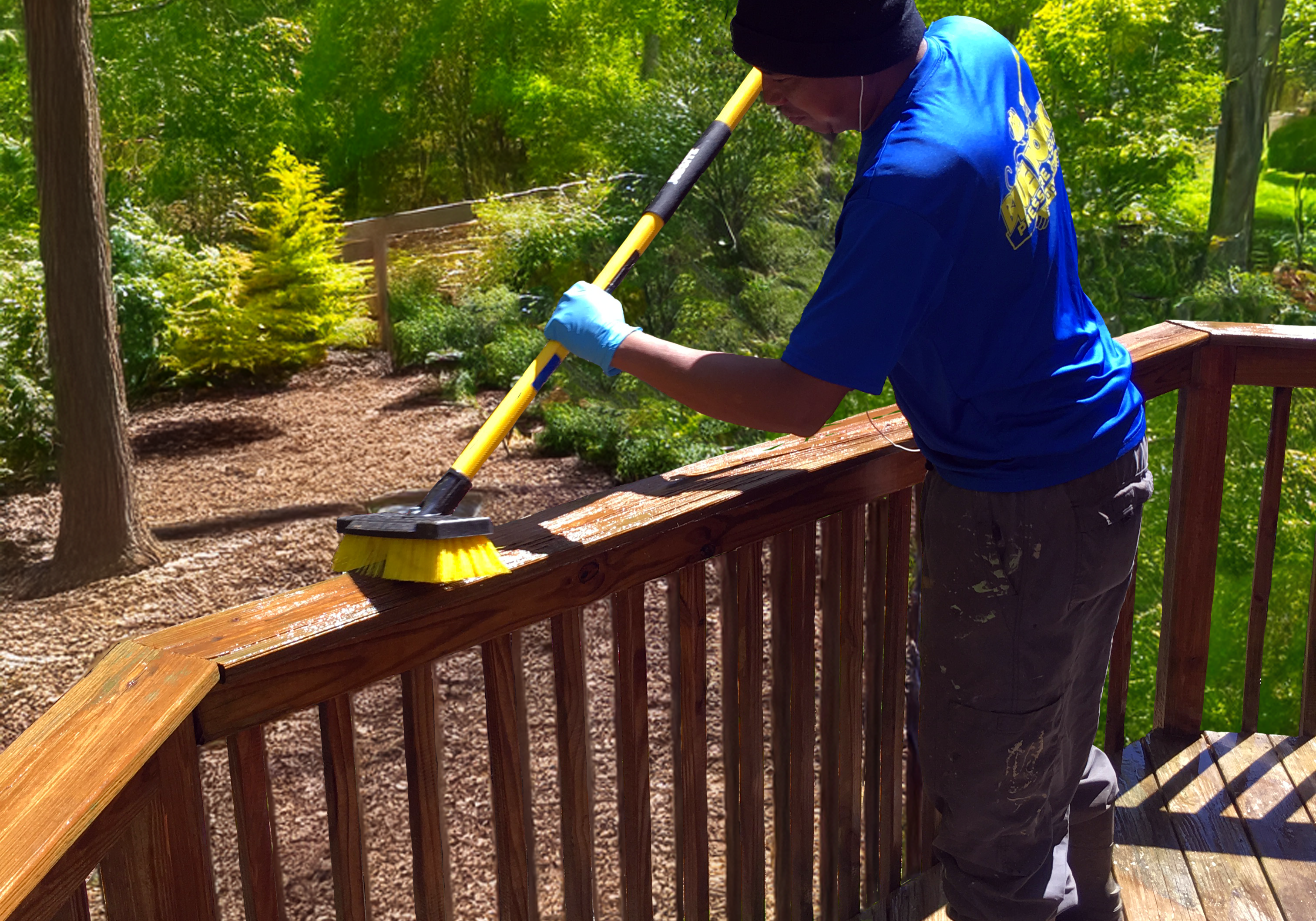 A man carefully hand-brushing stain onto a wooden deck railing, ensuring deep penetration and even coverage during DECK PRESSURE WASH, stain AND seal service