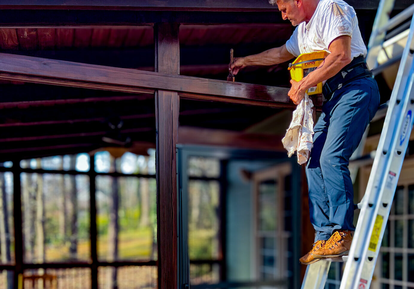 Expert Deck Staining & Restoration Services - MAN HAND BRUSHING STAINING THE TOP OF AN EXTERIOR DOOR FRAME