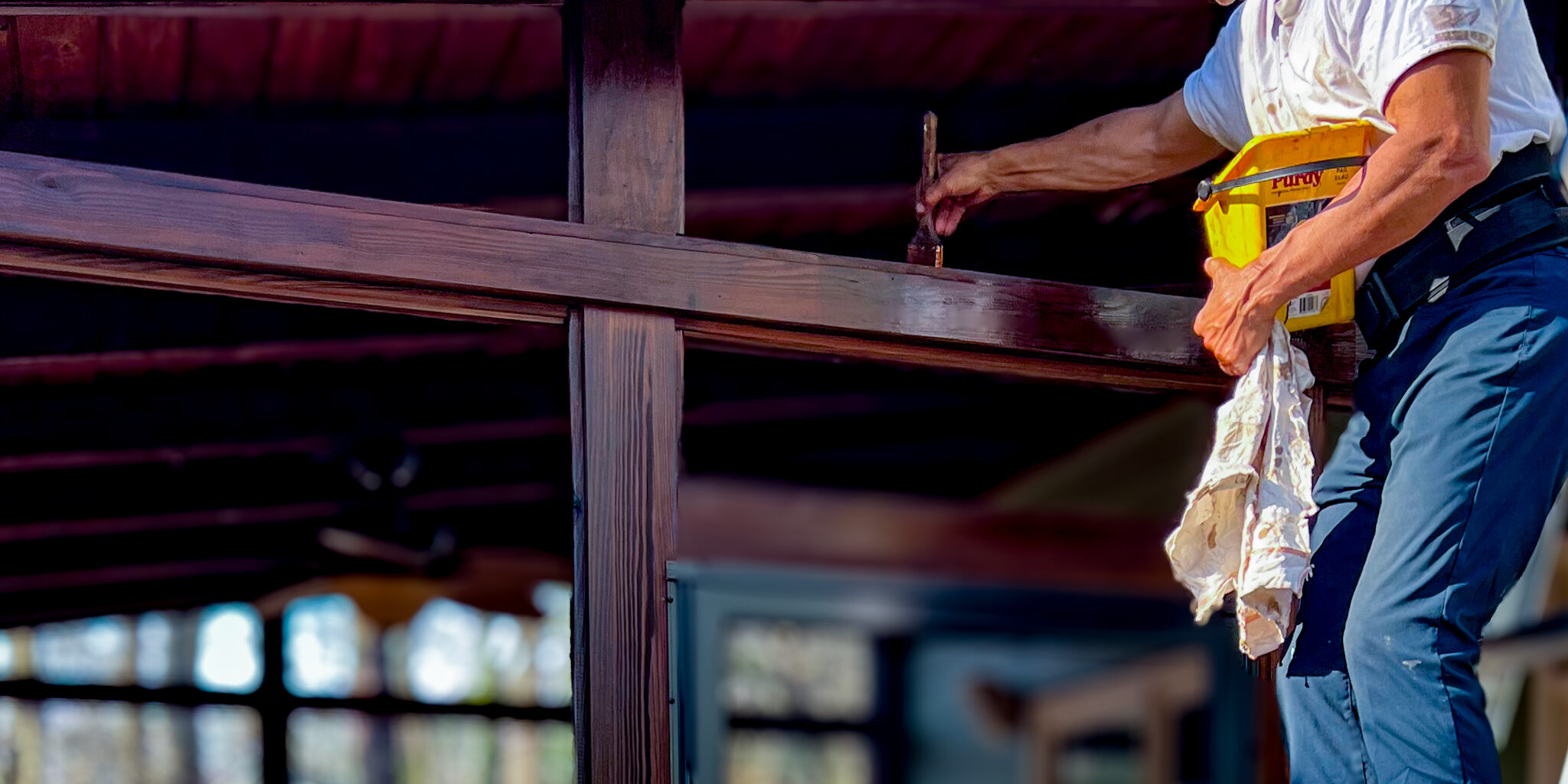 Expert Deck Staining & Restoration Services - MAN HAND BRUSHING STAINING THE TOP OF AN EXTERIOR DOOR FRAME