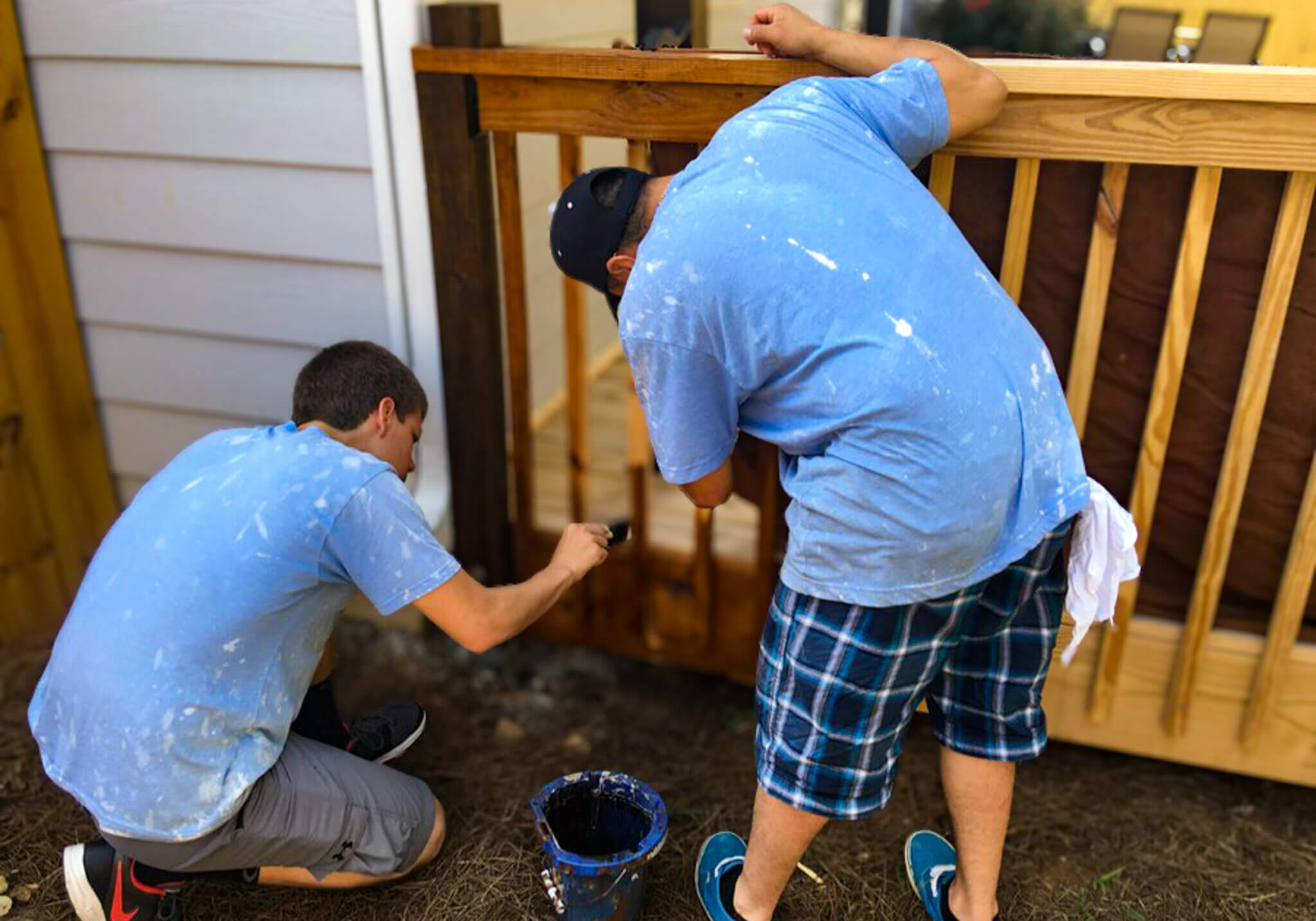 Two men staining and restoring a wooden deck railing, enhancing its durability and appearance with a professional finish.