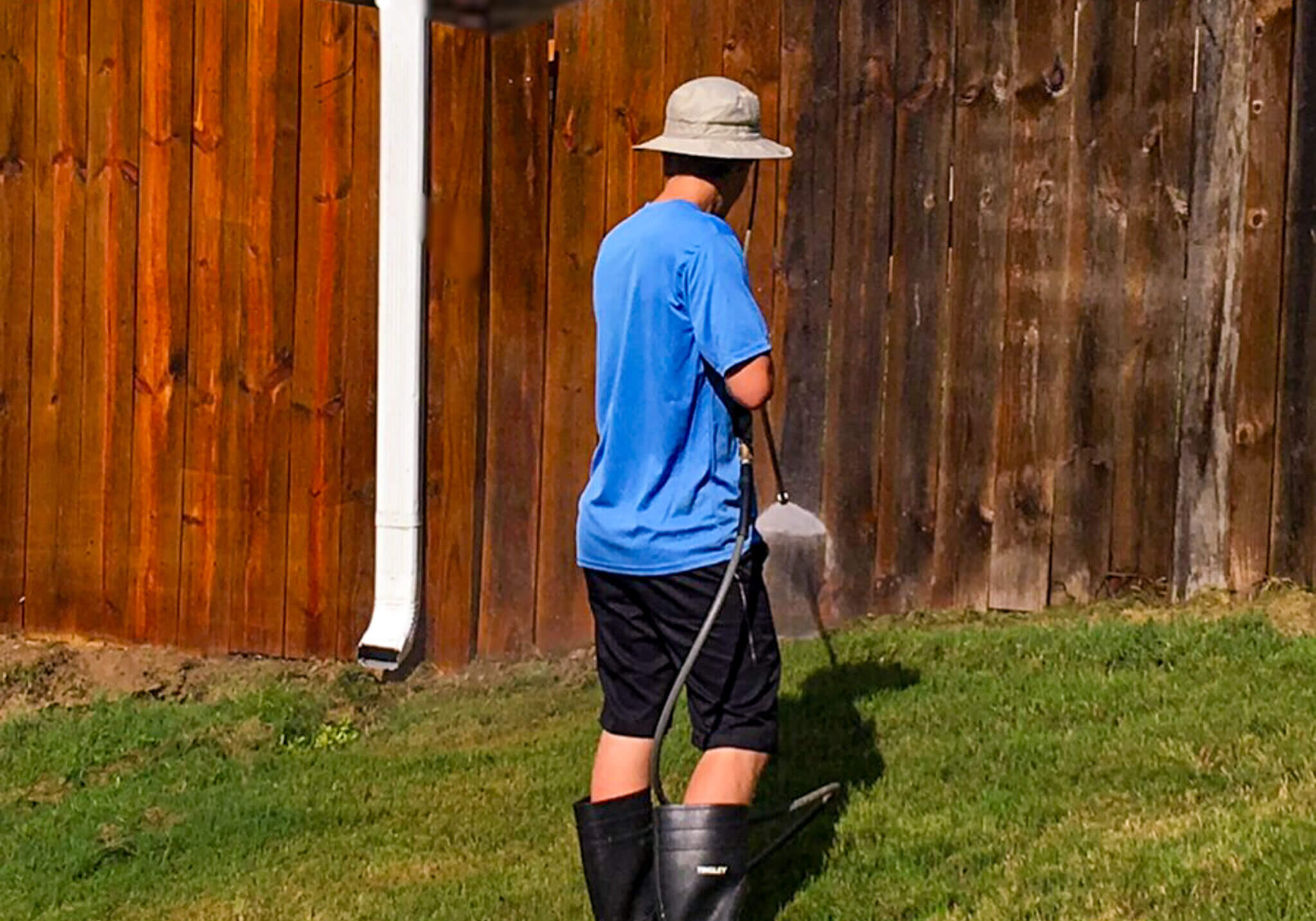 A worker pressure washing a wooden fence to remove dirt, grime, and old stain before applying a protective stain and seal.