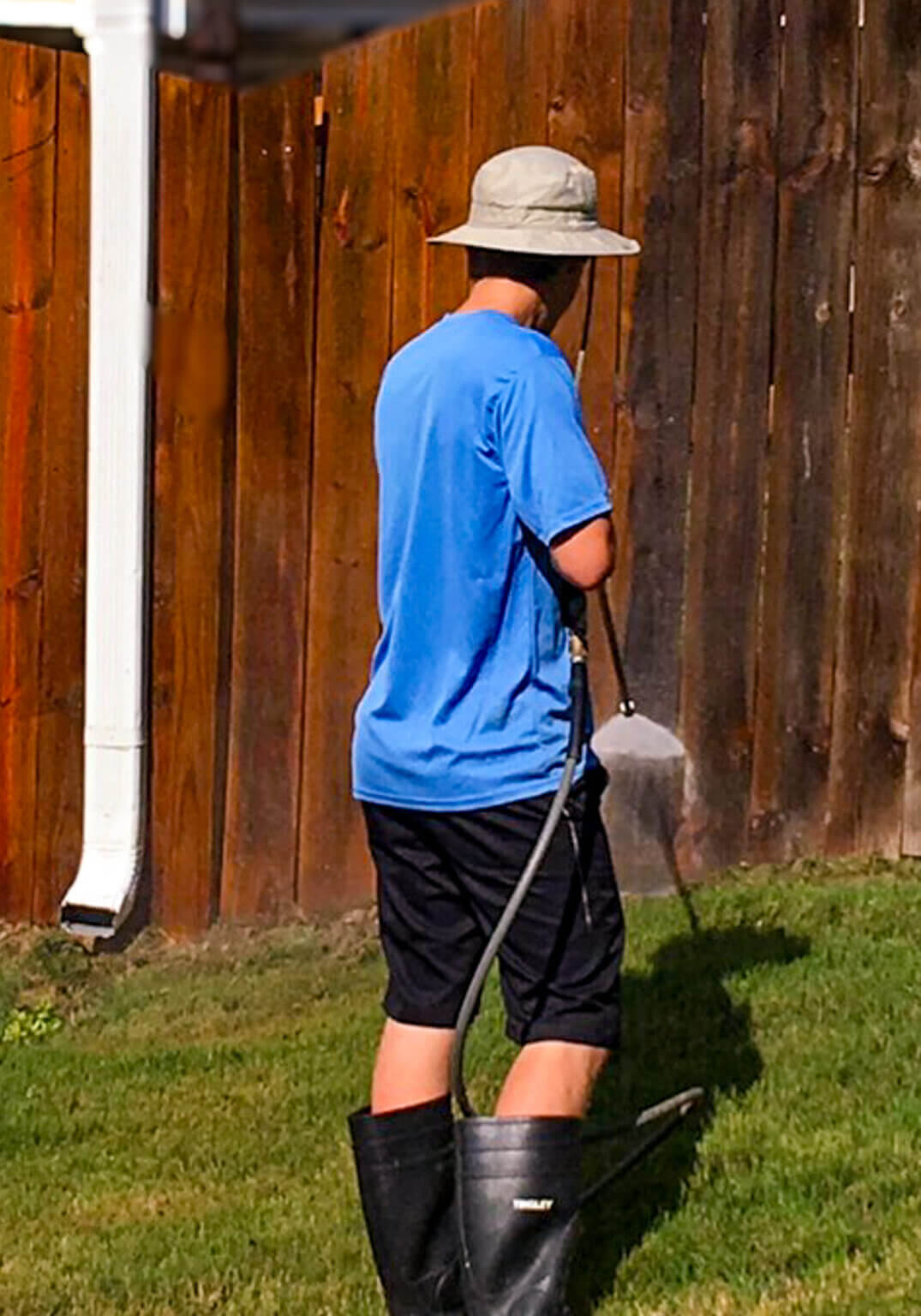 A worker pressure washing a wooden fence to remove dirt, grime, and old stain before applying a protective stain and seal.