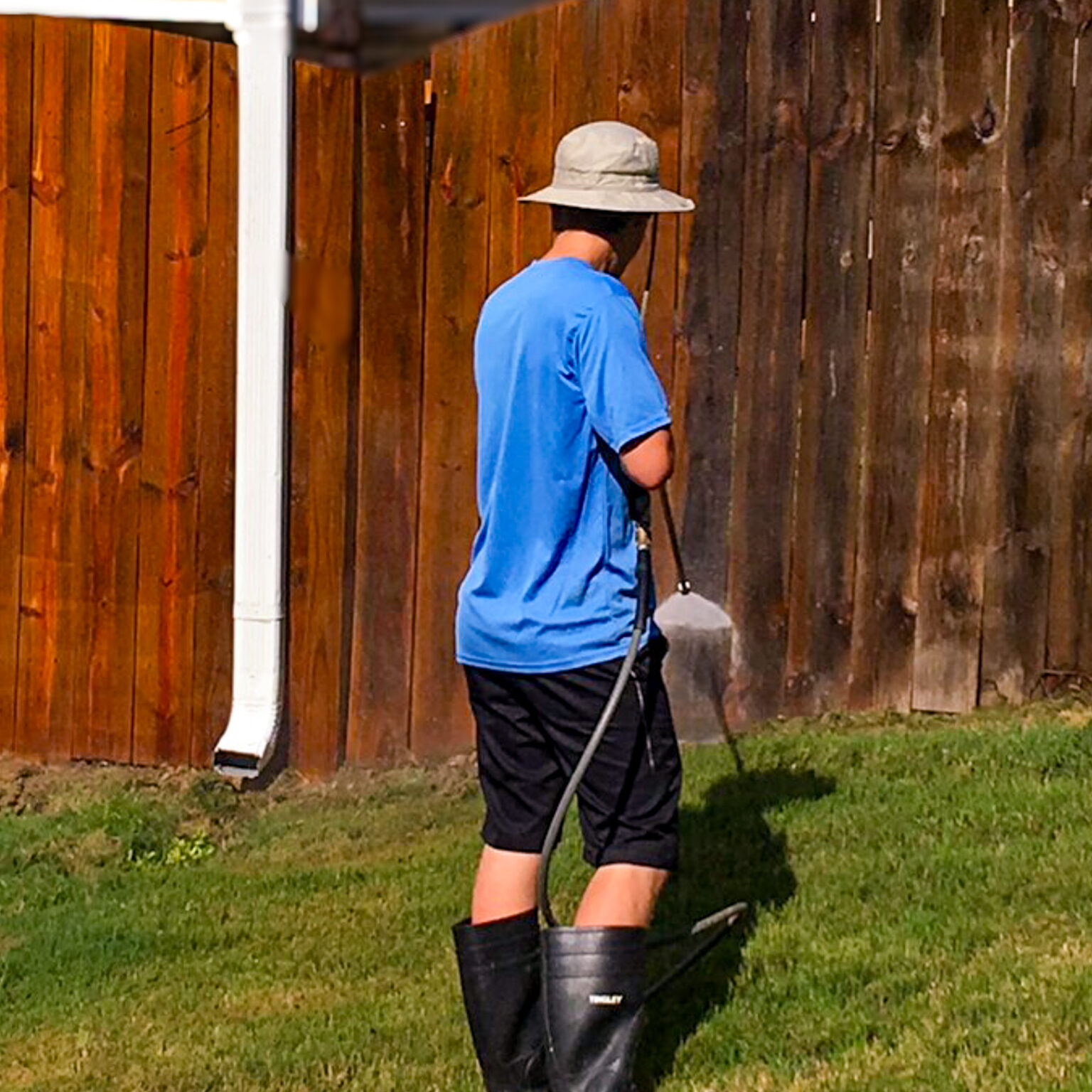 A worker pressure washing a wooden fence to remove dirt, grime, and old stain before applying a protective stain and seal.