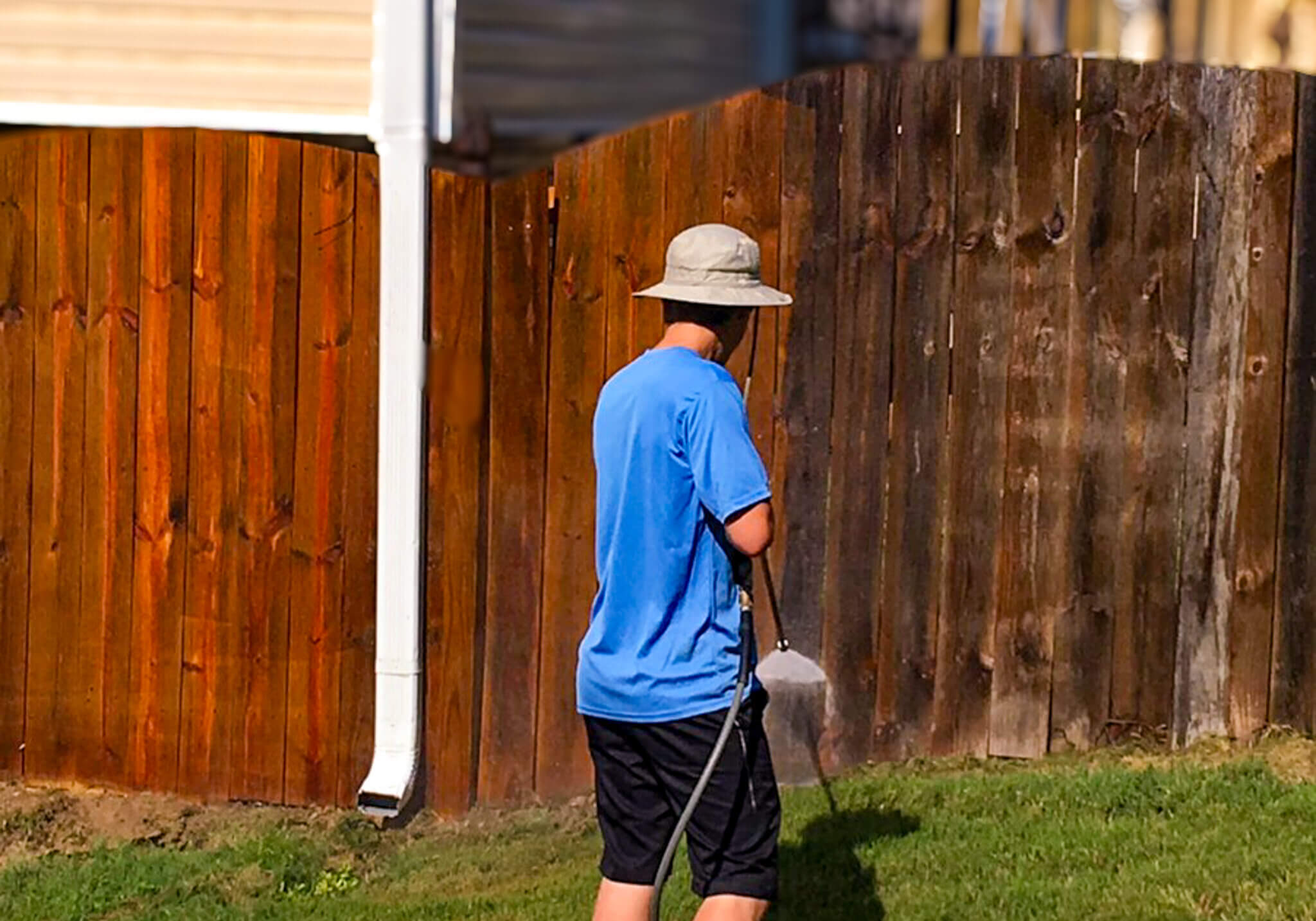 A worker pressure washing a wooden fence to remove dirt, grime, and old stain before applying a protective stain and seal. view our fence care services list