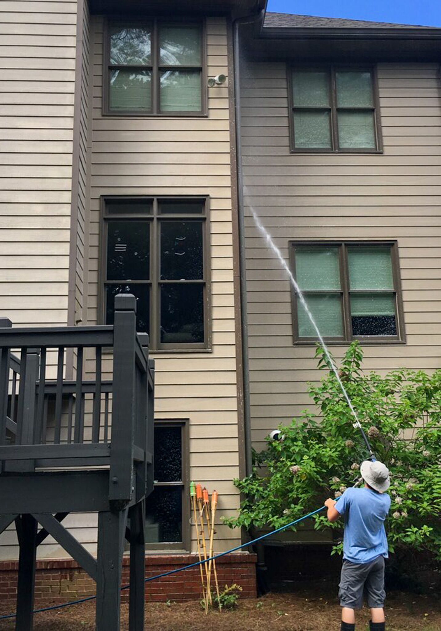 A cheerful Blue Monkey Pressure Washing technician using professional equipment to clean the exterior of a house, with water spraying and the house looking bright and spotless in the background.