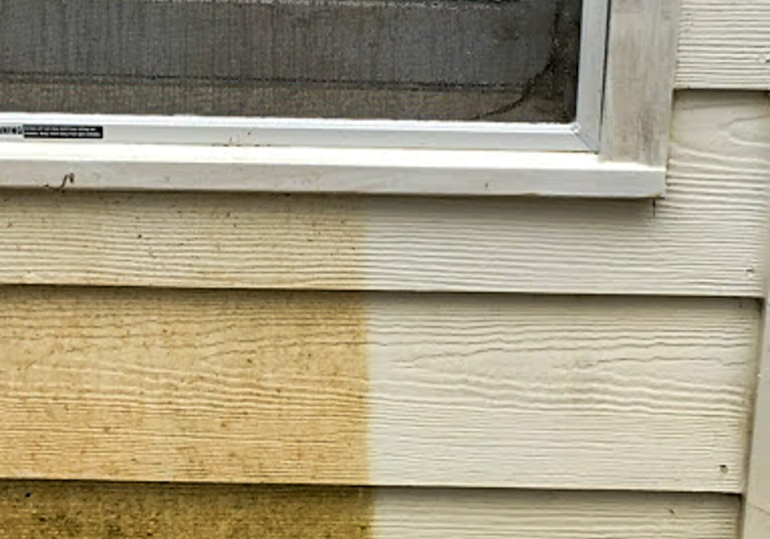 Wood siding being pressure washed, showing a clear contrast between the dirty surface and freshly cleaned exterior.