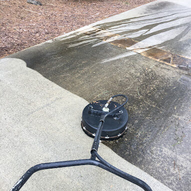 Pressure washing tool on a concrete driveway mid-cleaning, showing a clear line between dirty and freshly cleaned concrete surface. PREP CONCRETE FOR SEALING SERVICE